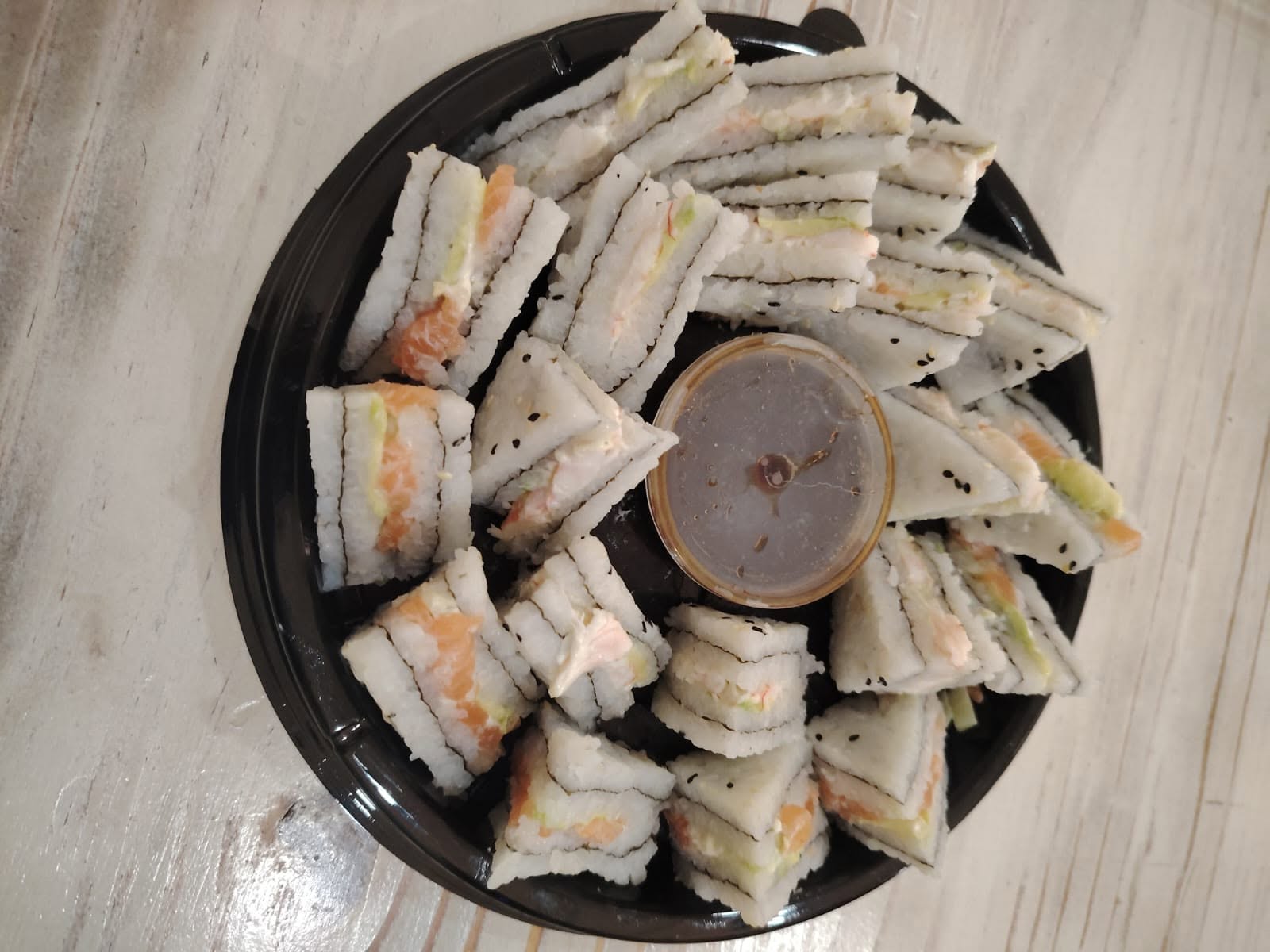 Fashion Sandwich Platter — triangular sushi sandwiches with salmon, avocado and crab salad arranged around a central soy sauce cup on a round black tray.