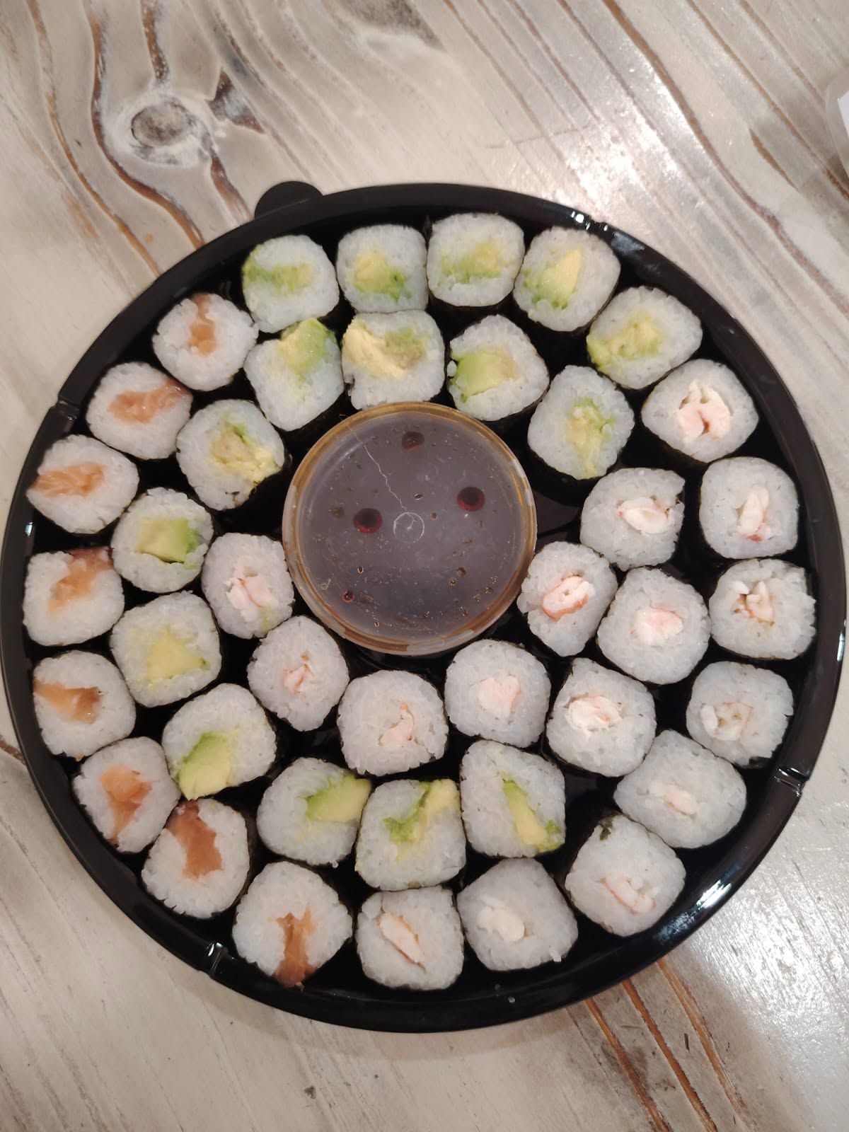 Maki Rolls Platter — assorted avocado, salmon and prawn maki arranged in concentric circles on a round black tray.